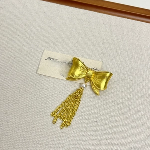 Detail of vintage gold bow brooch featuring a white pearl and elegant metal fringe chains