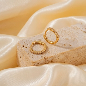 Detailed close-up of golden hoop earrings with white zircon on beige stone and silk