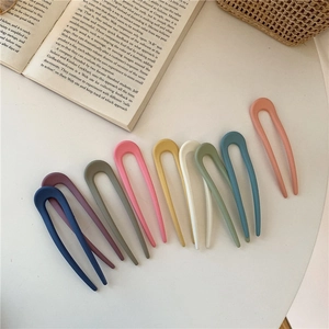 Flat lay of eight colorful matte U-shaped hair pins on a white table with an open book