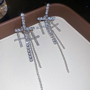 Detailed view of silver cross earrings with dangling metal chains and shimmering zircons