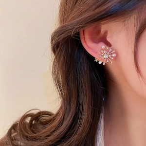 Close-up of golden starburst earrings with pearls and crystals worn by a model
