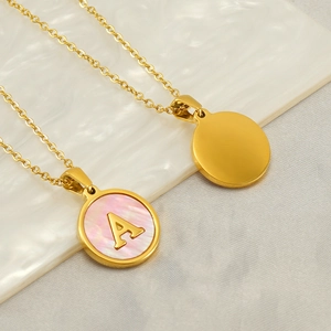 Colliers avec lettre A en nacre rose et pendentif disque doré sur marbre blanc
