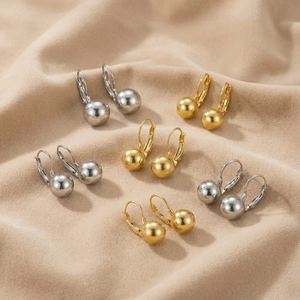 Detail of polished gold and silver ball drop earrings on warm beige velvet fabric