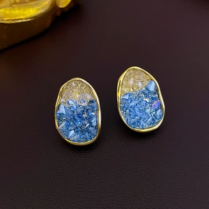 Macro detail of gold-plated earrings with gradient yellow and blue crystal inlay