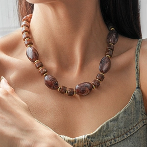 Gros plan de perles en acrylique marbré et d'anneaux dorés sur un collier vintage chic