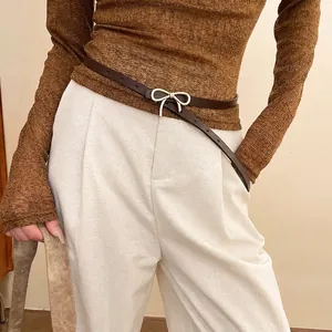 Vintage brown leather skinny belt with golden bow buckle on white trousers