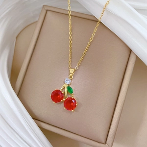 Macro detail of red cherry pendant with crystal leaf on gold titanium steel chain