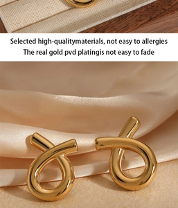 Close-up of gold geometric fish-shaped earrings on elegant beige silk fabric background