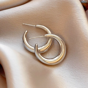 Macro view of polished silver hoop earrings on elegant silk fabric background