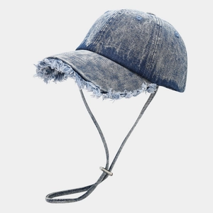 Dettaglio del cappellino in denim con tesa sfilacciata e cordino antivento regolabile