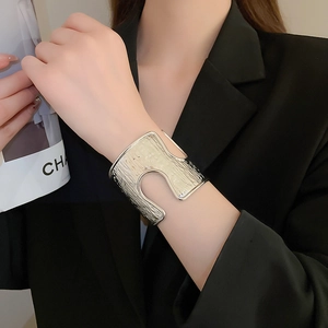 Detail of silver-colored wide open cuff bracelet with vertical texture on black blazer