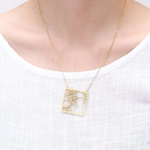 Detail of a square cutout city map pendant in gold finish worn by a model