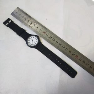 Flat lay of silent quartz exam watch with black strap beside a metal ruler for size