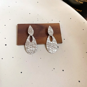 Detailed macro view of textured oval drop earrings with irregular metallic surface details