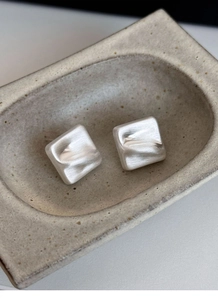 Macro shot of silver square stud earrings with brushed texture on ceramic dish