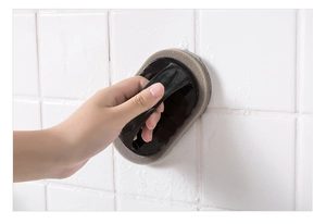 Handheld emery sponge cleaning brush with ergonomic handle used on white tiled wall