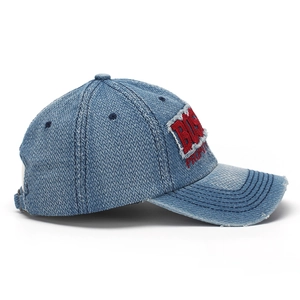 Détail de la casquette baseball en denim délavé avec broderie rouge 3D et bords usés
