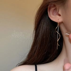 Detail of elegant gold wave chain tassel drop earrings on model for a minimalist look