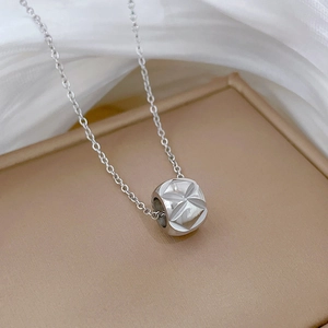 Close-up of a silver cylinder pendant with geometric facets on a thin necklace chain