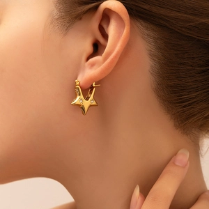 Detailed close-up of a gold star hoop earring with cubic zirconia on a model's ear
