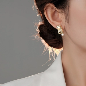 Close-up of model wearing square pearl stud earring with irregular gold lava texture