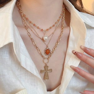Detail of layered gold necklace with pearl, orange gemstone and cross pendant on model