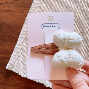 Close-up of a cream-colored crinkle bow hair clip on a soft pink display card