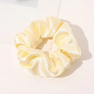 Close-up of a pale yellow silk satin scrunchie with elegant folds and shiny texture