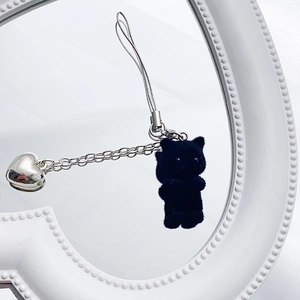 Close-up of black flocked cat keychain with silver heart pendant on white heart decor