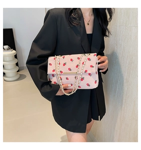 Détail du sac bandoulière en velours côtelé rose avec broderie fraise et chaîne dorée