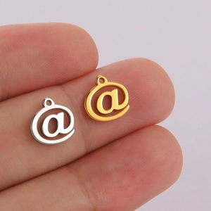 Polished stainless steel @ symbol charms in gold and silver finish held by hand