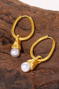 Detailed shot of gold oval earrings with white teardrop pearls on a vintage wood texture