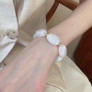 Detailed macro view of irregular white marble resin beads and golden metal spacers on the wrist