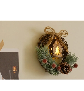 Detail of Christmas wreath featuring a glowing wooden house with pine cones and red berries