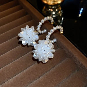 Dettaglio di orecchini a petalo bianco con frange di perle e finiture in metallo oro