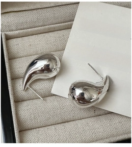 Close-up of teardrop silver earrings in a beige velvet jewelry box with Roman card