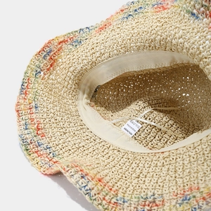 Detail of hand-woven straw hat showing 100% paper material label and colorful rim stitching