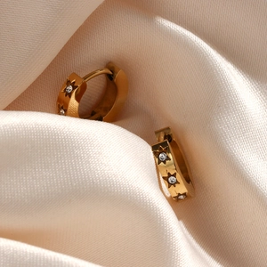 Macro view of 18K gold plated star hoop earrings with zircons on beige silk fabric