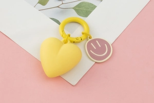 Detailed view of yellow heart keychain with a cartoon smiley face charm on a pink background