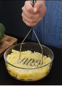 Presse-purée en acier inoxydable écrasant des légumes dans un bol en verre