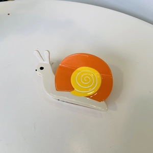 Detail of snail-shaped acetate hair claw clip featuring bright orange and yellow shell pattern