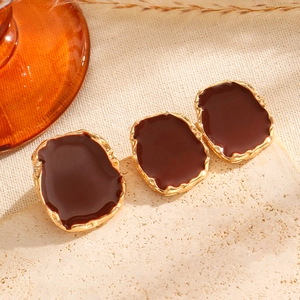 Close-up of vintage irregular gold earrings with brown drip glaze on stone surface