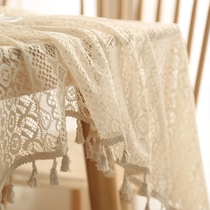 Close-up of beige lace tablecloth corner with hollow flower patterns and tassel details