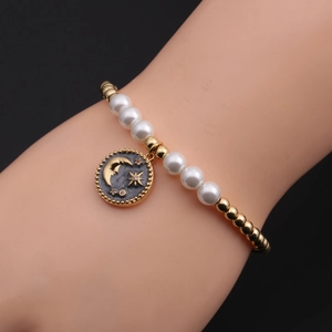 Detailed shot of gold plated bracelet featuring moon and star charm with white faux pearls