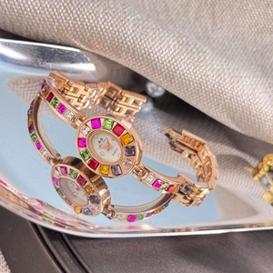 Macro shot of rose gold quartz watch with colorful zircon on a silver reflective tray