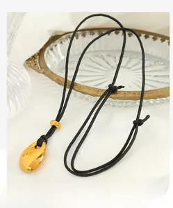 Macro shot of polished gold water drop pendant with adjustable black braided cord