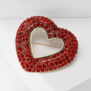 Detail view of heart brooch with red rhinestones and gold base on a white background