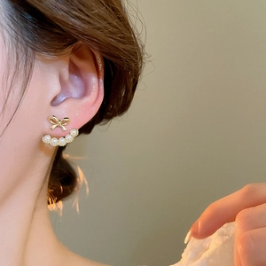 Close-up of 18k gold-plated bow pearl earrings worn on ear with elegant details