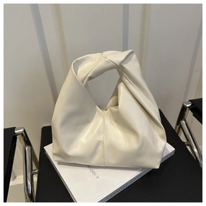 Detail of minimalist cream tote bag showing the unique knot handle and draped leather