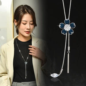 Detail of flower pendant necklace with blue stones and metal tassel on a model